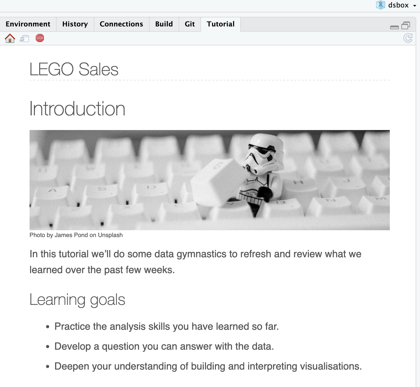 The image is a screenshot of a computer application, the RStudio IDE, with black text on a white background and a large image in the center. At the top, the title says "LEGO Sales." The image consists of a Stormtrooper LEGO minifigurine on a white computer keyboard. The text below the image describes the purpose of the tutorial (to review previous concepts on data wrangling) and the goals (practice the analysis skills learned so far, developing questions in the data, and deepening the understanding of visualizations.)